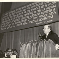 Cesare Campioli parla in occasione di una manifestazione pubblica unitaria antifascista. Sul palco si riconoscono Alcide Cervi a sinistra e Franco Boiardi con gli occhiali, verso il centro