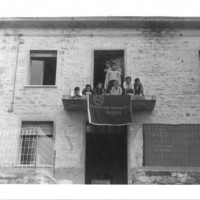 Gruppo di giovani donne affacciate a un balcone, con la bandiera della federazione modenese della FGCI
[ISMO, AFPCMO]